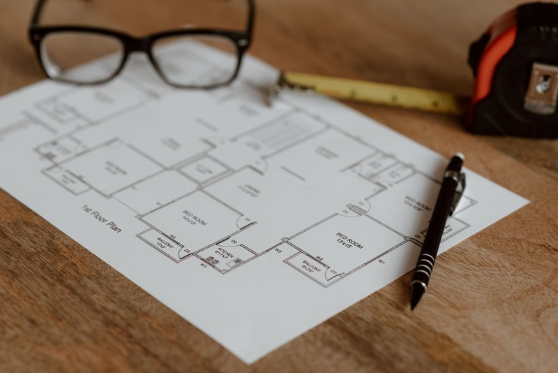 Grundriss mit Brille, Zollstock und Bleistift auf einem Holztisch